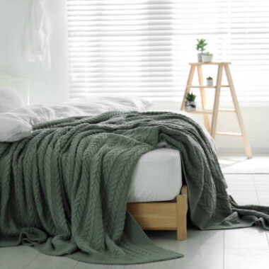 Comfortable bed with warm knitted plaid in stylish room interior