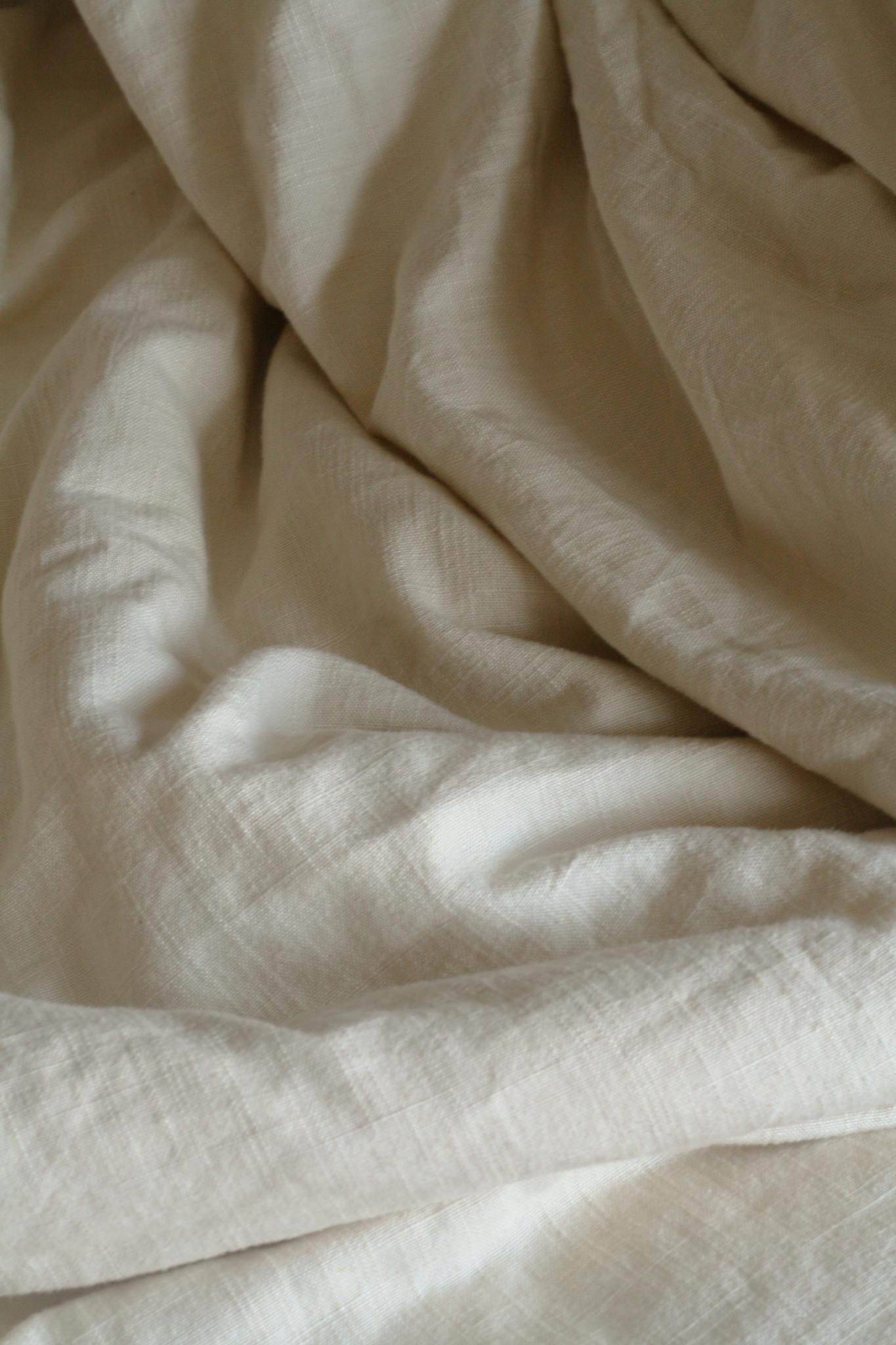 Soft and textured beige linen bedding fabric forming natural folds, perfect for interior decor themes.